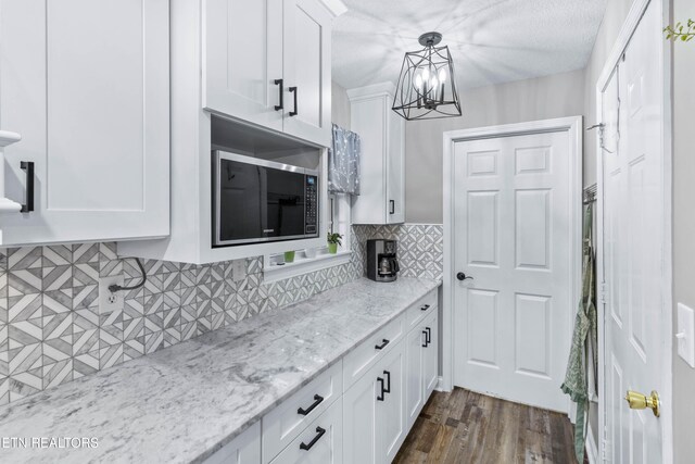 kitchen with pendant lighting, dark hardwood / wood-style floors, decorative backsplash, light stone counters, and white cabinetry