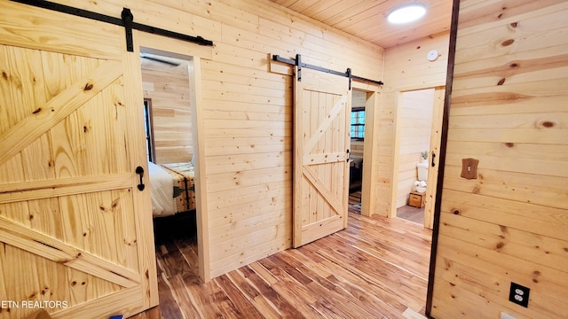 corridor featuring a barn door, wood walls, hardwood / wood-style floors, and wooden ceiling