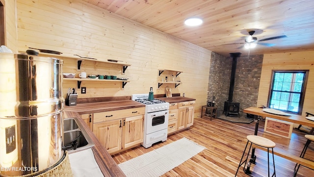 kitchen with a wood stove, gas range gas stove, wood counters, light hardwood / wood-style floors, and wooden walls