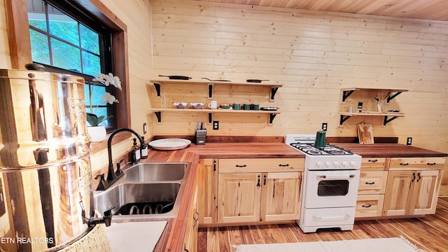 kitchen with gas range gas stove, sink, wooden counters, wooden walls, and light wood-type flooring