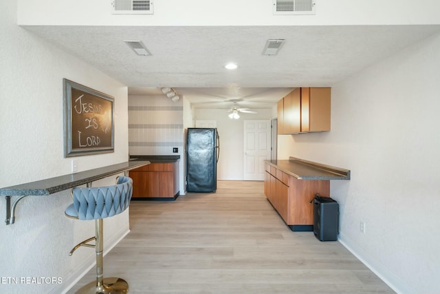 kitchen featuring track lighting, black refrigerator, light hardwood / wood-style flooring, ceiling fan, and a textured ceiling