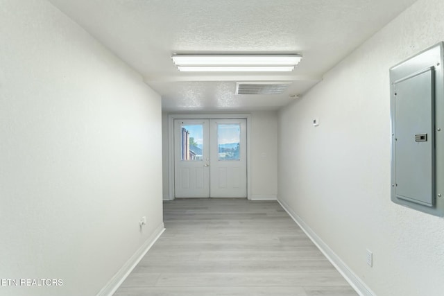 hall featuring electric panel, french doors, light hardwood / wood-style floors, and a textured ceiling