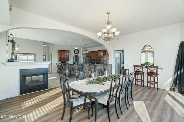 dining room featuring a multi sided fireplace, light wood-type flooring, and a notable chandelier