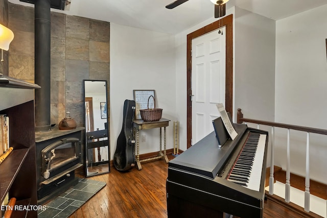 misc room featuring a wood stove, ceiling fan, dark hardwood / wood-style flooring, and tile walls