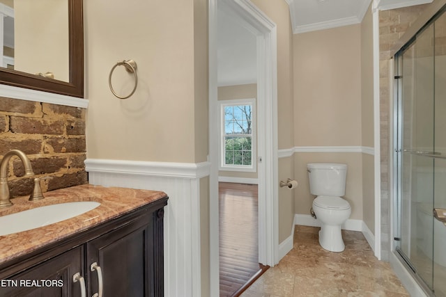 bathroom with vanity, toilet, a shower with shower door, and crown molding