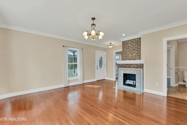 unfurnished living room with a brick fireplace, crown molding, wood-type flooring, and a notable chandelier