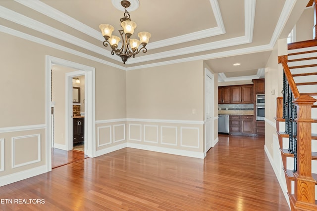 unfurnished dining area with hardwood / wood-style floors, a tray ceiling, an inviting chandelier, and ornamental molding