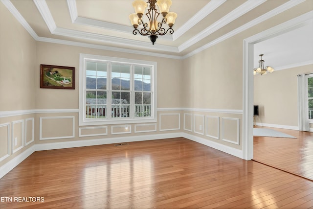 empty room featuring crown molding, an inviting chandelier, a healthy amount of sunlight, and wood-type flooring