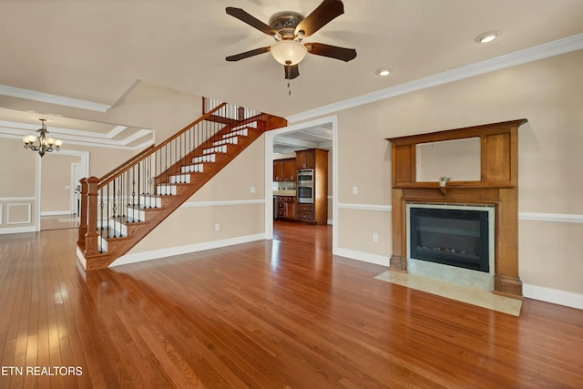 unfurnished living room with hardwood / wood-style flooring, ceiling fan with notable chandelier, ornamental molding, and a premium fireplace