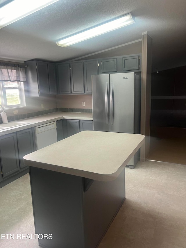 kitchen with gray cabinetry, sink, white dishwasher, vaulted ceiling, and a kitchen island