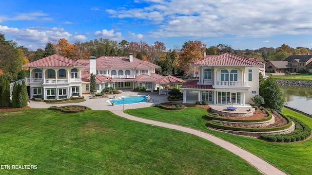 back of property featuring a lawn, a patio area, a balcony, and a water view