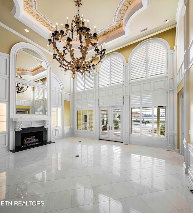 unfurnished living room featuring a high ceiling, an inviting chandelier, light tile patterned floors, ornamental molding, and a premium fireplace