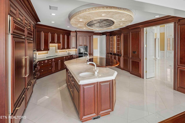 kitchen featuring sink, paneled fridge, black electric cooktop, a center island with sink, and light tile patterned flooring