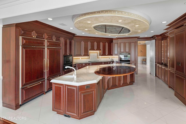 kitchen with light stone counters, a kitchen island with sink, crown molding, sink, and black appliances