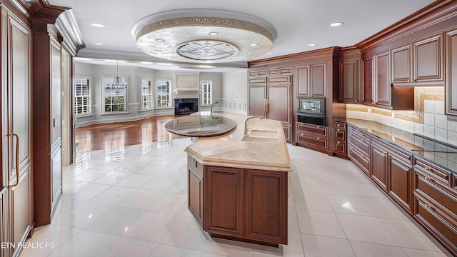 kitchen featuring dark stone counters, sink, crown molding, light tile patterned floors, and an island with sink