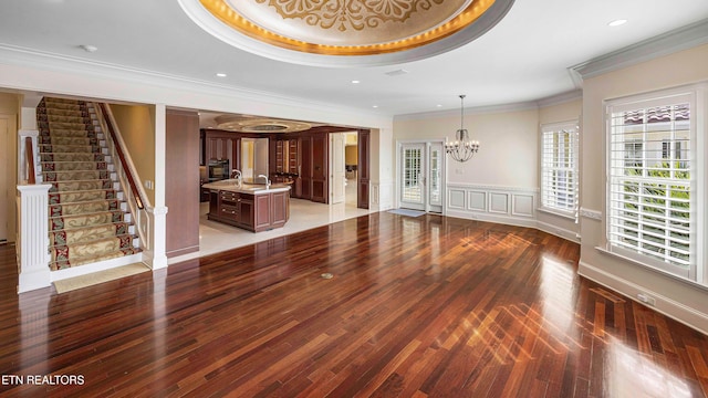 unfurnished living room featuring a tray ceiling, crown molding, sink, a notable chandelier, and dark hardwood / wood-style floors