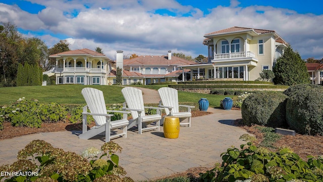 rear view of property with a balcony, a yard, and a patio