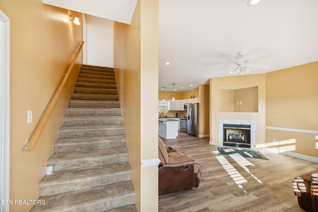 stairway with ceiling fan, wood-type flooring, and a tiled fireplace