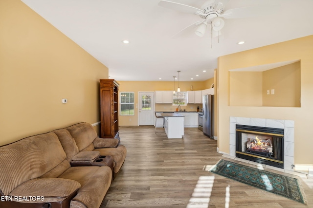 living room with a tile fireplace, light hardwood / wood-style flooring, ceiling fan, and sink