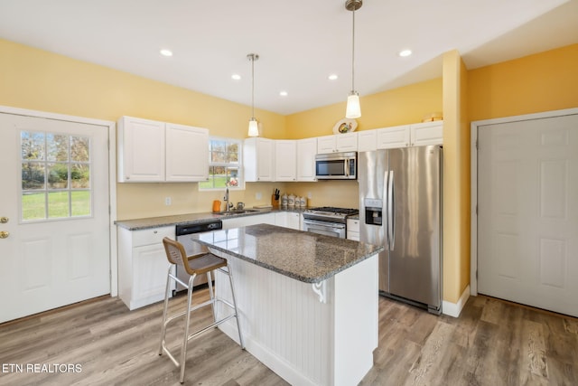 kitchen with a center island, dark stone counters, light hardwood / wood-style flooring, appliances with stainless steel finishes, and white cabinetry