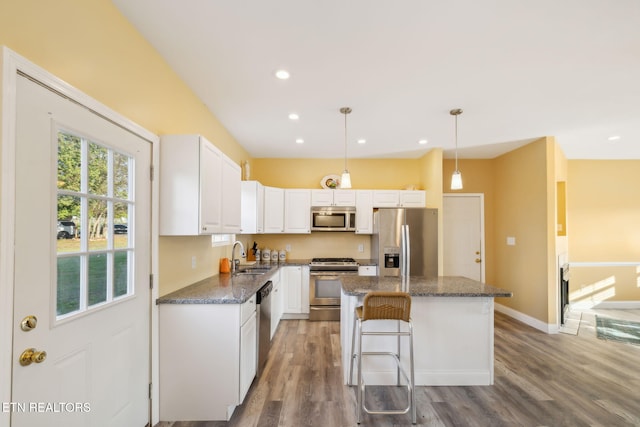 kitchen featuring stainless steel appliances, dark stone countertops, hardwood / wood-style floors, pendant lighting, and a kitchen island