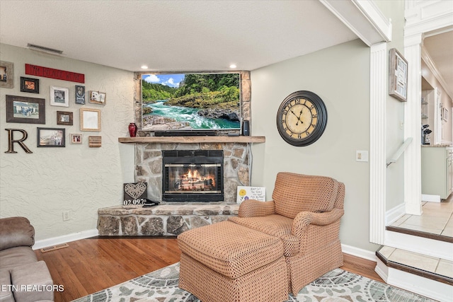 living room with a textured ceiling, light wood-type flooring, and a stone fireplace