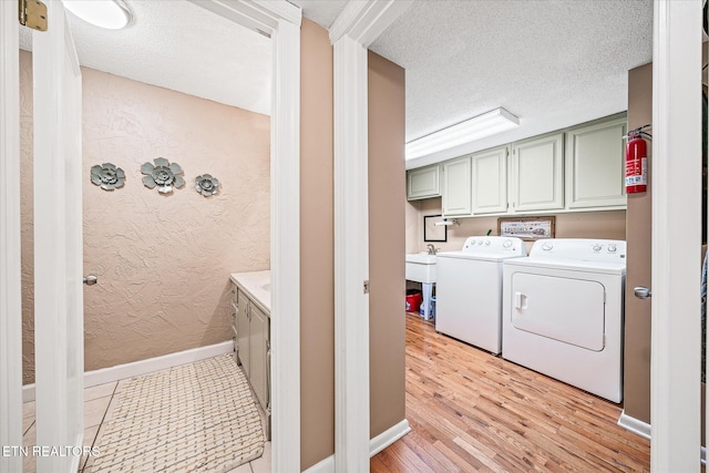 laundry area featuring washer and dryer, a textured ceiling, cabinets, and light hardwood / wood-style flooring