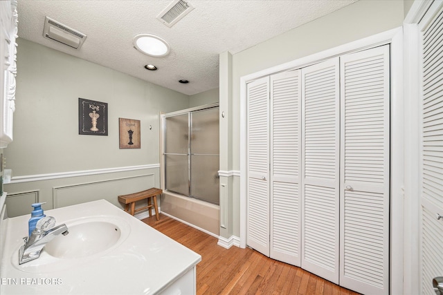 bathroom featuring a textured ceiling, enclosed tub / shower combo, vanity, and hardwood / wood-style flooring