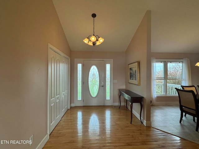 foyer entrance with light wood-type flooring, high vaulted ceiling, and an inviting chandelier