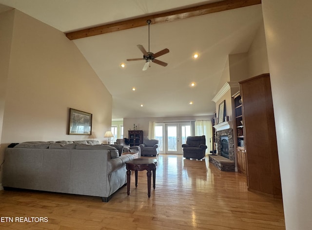 living room with beam ceiling, a stone fireplace, light wood-type flooring, and high vaulted ceiling