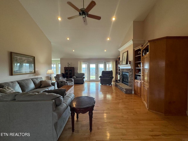 living room featuring high vaulted ceiling, french doors, a stone fireplace, light hardwood / wood-style flooring, and ceiling fan