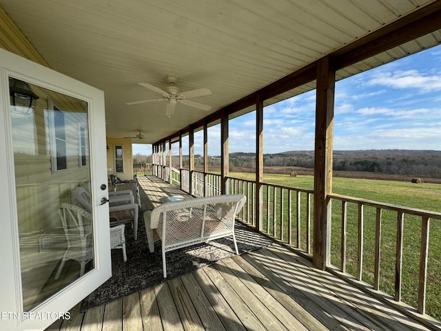 wooden deck featuring a rural view, ceiling fan, and a lawn