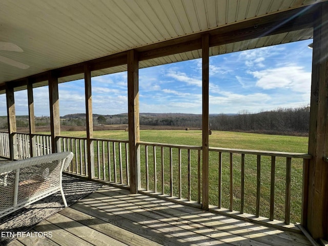 wooden terrace with ceiling fan, a yard, and a rural view