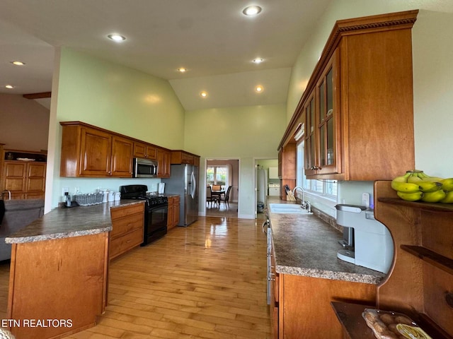 kitchen with high vaulted ceiling, sink, light wood-type flooring, appliances with stainless steel finishes, and kitchen peninsula