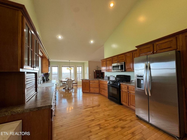 kitchen with pendant lighting, high vaulted ceiling, sink, light hardwood / wood-style floors, and stainless steel appliances