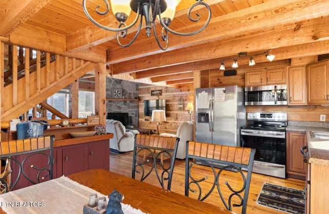 kitchen featuring beamed ceiling, appliances with stainless steel finishes, light wood-type flooring, and a stone fireplace