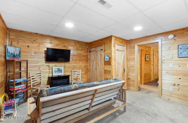 carpeted living room featuring a drop ceiling and wood walls