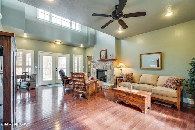 living room featuring french doors, a towering ceiling, ceiling fan, hardwood / wood-style flooring, and a fireplace