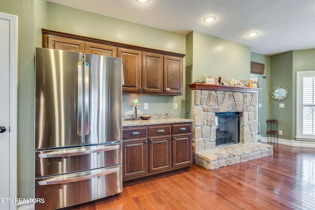 kitchen with hardwood / wood-style floors, a textured ceiling, stainless steel refrigerator, and a stone fireplace