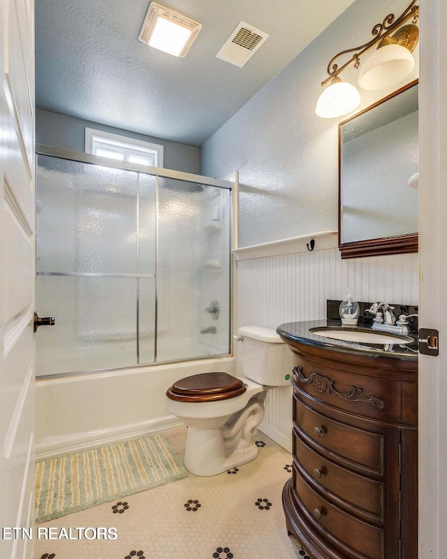 full bathroom with combined bath / shower with glass door, a textured ceiling, vanity, tile patterned flooring, and toilet