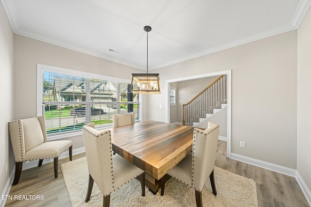 dining space with crown molding, an inviting chandelier, and light wood-type flooring