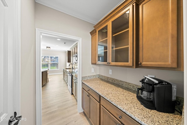 kitchen featuring light stone countertops, light wood-type flooring, stainless steel appliances, crown molding, and sink