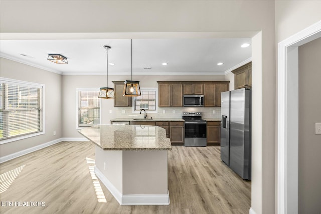 kitchen featuring appliances with stainless steel finishes, light hardwood / wood-style floors, a wealth of natural light, and pendant lighting