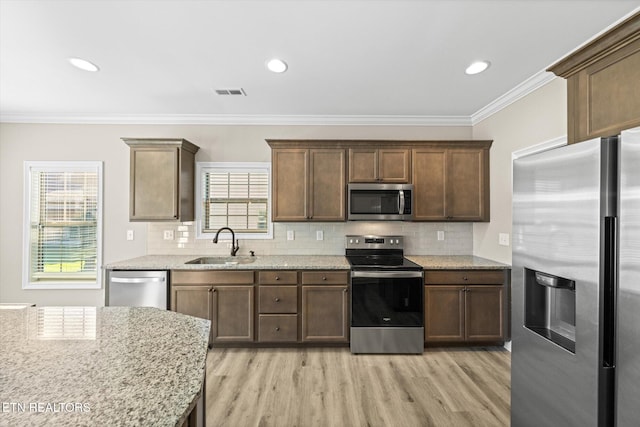 kitchen featuring appliances with stainless steel finishes, light wood-type flooring, light stone counters, ornamental molding, and sink