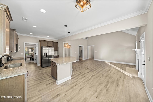 kitchen with light wood-type flooring, light stone counters, stainless steel appliances, sink, and a kitchen island