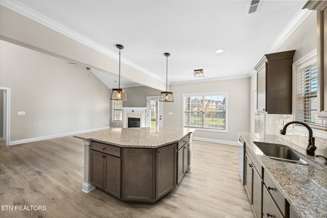 kitchen featuring light wood-type flooring, light stone counters, ornamental molding, and sink