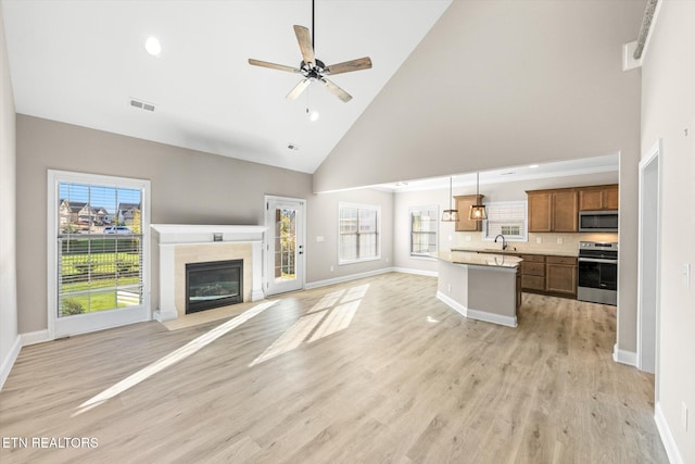 unfurnished living room featuring a tiled fireplace, high vaulted ceiling, a healthy amount of sunlight, and light hardwood / wood-style floors