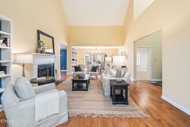 living room with a chandelier, built in shelves, light hardwood / wood-style floors, and high vaulted ceiling