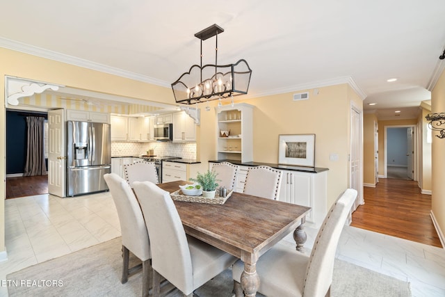 dining room with a chandelier, light wood-type flooring, and ornamental molding