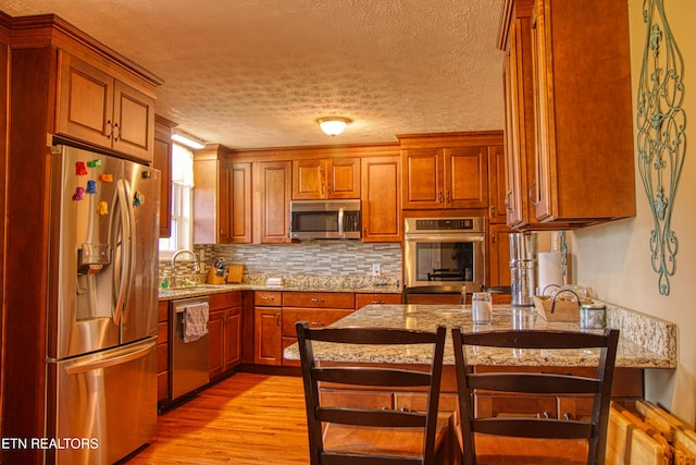 kitchen with sink, stainless steel appliances, light stone counters, light hardwood / wood-style floors, and a textured ceiling